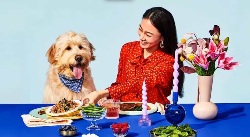 Woman sitting at the table with her dog eating chicken-free dog food