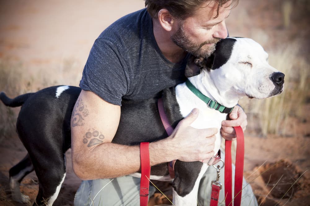 Owner petting and snuggling dog holding leash outside