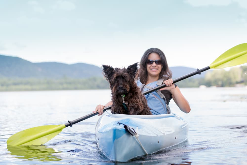 Woman sits in a kayak paddling with her dog