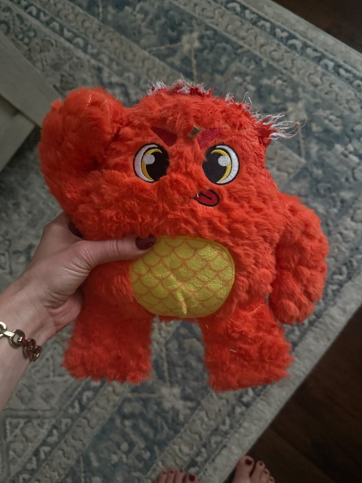 Hand holding orange Bite Force plush toy with yellow belly.