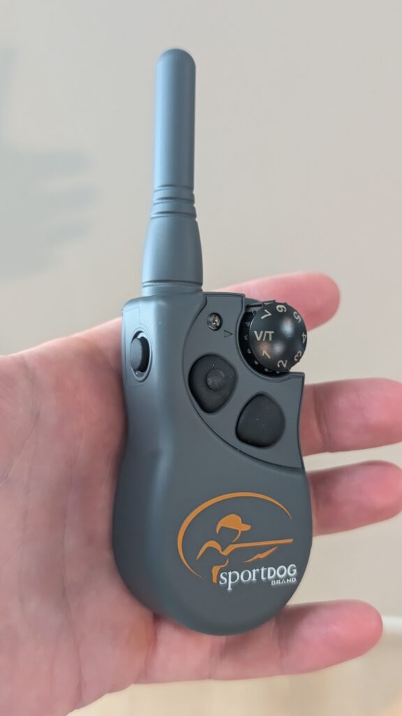 Hand holding the SportDOG FieldTrainer 425X transmitter with its top dial and side buttons