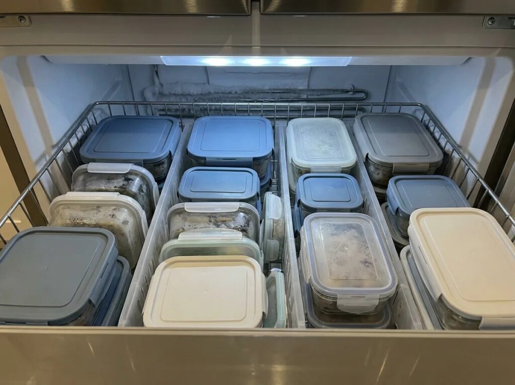 Lidded reusable food containers organized inside a freezer drawer.