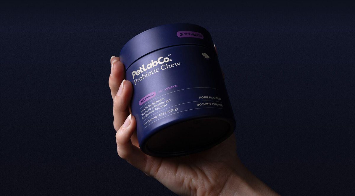 A hand holds a PetLabCo. Probiotic Chew tub against a dark background.